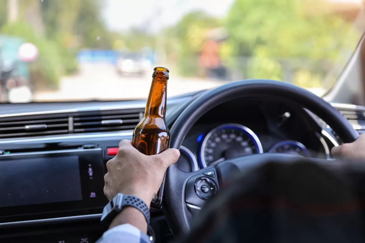 Moški vozi avto in drži steklenico alkohola